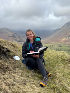 Victoria Rose Miller sitting on a hillside sketching